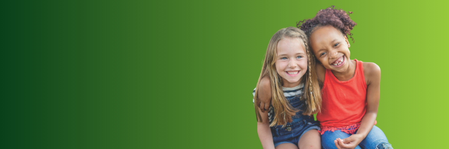 Two smiling girls sit close together against a green gradient background, posing for a friendly photo.