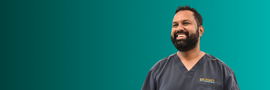 Smiling man with a dark beard in gray scrubs against a teal gradient background.