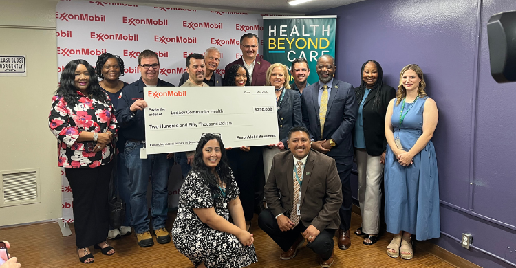 Group photo at a donation ceremony: ExxonMobil presents a large check to Legacy Community Health, with a 'Health Beyond Care' banner in the background.