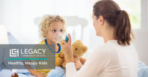 Child receives a nebulizer treatment from a clinician in a bright clinic, with a teddy bear nearby and the Legacy Healthy, Happy Kids logo visible in the foreground.