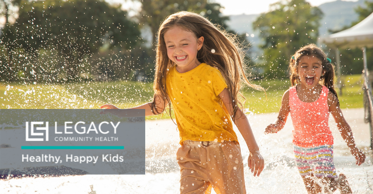 Two smiling kids running through water jets in a sunny park, with a Legacy Community Health logo and the slogan 'Healthy, Happy Kids' overlaid on the image.