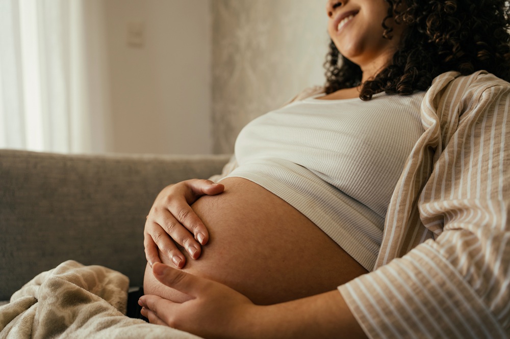Pregnant woman resting on a couch, hands cradling her baby bump and smiling slightly.