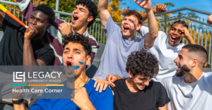 Group of diverse young men cheering outdoors, with the Legacy Community Health logo in the corner indicating a health outreach event.
