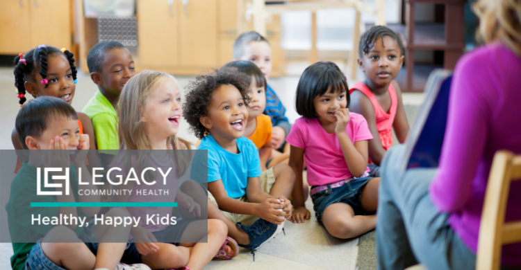 Diverse group of children sitting on the floor, listening to a reader in a classroom; Legacy Community Health branding and 'Healthy, Happy Kids' slogan visible.