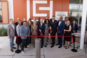 Group of community leaders, elected officials, healthcare leaders and partners participate in a ribbon-cutting ceremony outside the Legacy Community Health Acres Homes Clinic in Houston. Participants stand behind a red ribbon in front of the clinic entrance and Houston Methodist recognition signage.