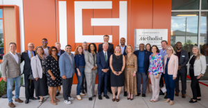 A diverse group of people stands in front of a modern building with a large "LCH" logo. A sign shows appreciation to Houston Methodist Hospital Foundation. The individuals are smiling and dressed in business casual and formal attire.